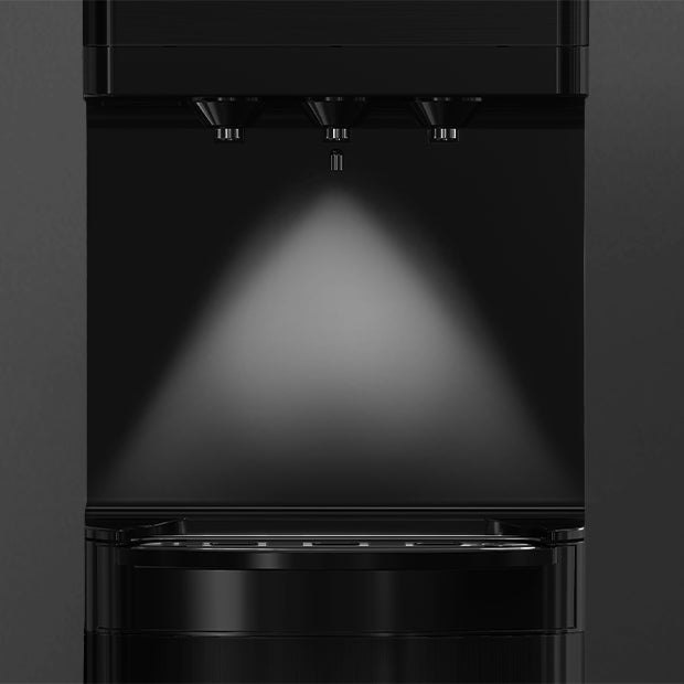 Close-up of a modern, black coffee or beverage dispenser with three spouts and a lit area below, illuminating the dispensing zone. The design is sleek and minimalistic.